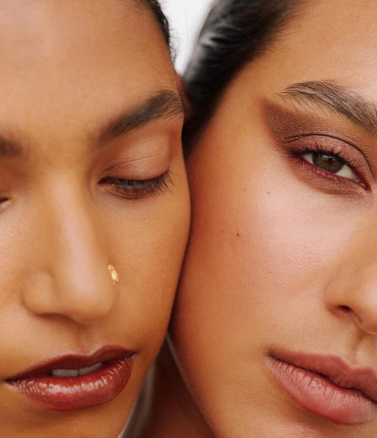 Close-up shot featuring the faces of two adult women with different skin tones, showcasing beauty and makeup in a minimalist style.