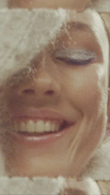 Close-up portrait of a smiling adult female with soft makeup and a white, fluffy head covering, showcasing a beauty and fashion aesthetic.