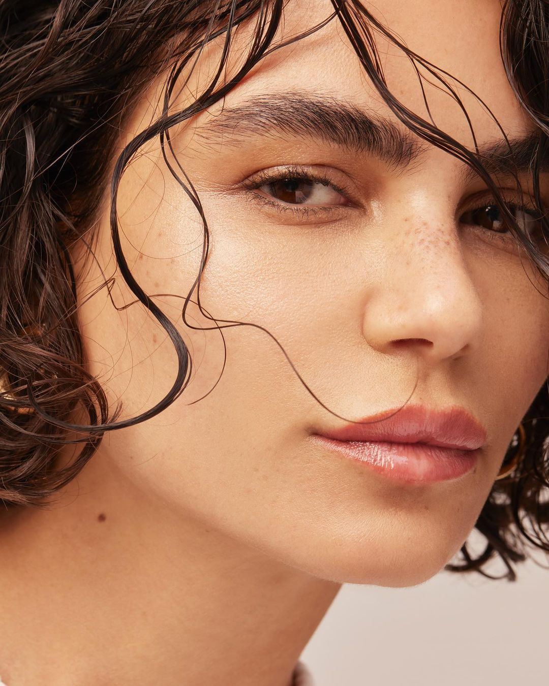 Close-up portrait of an adult female with wet, short, dark hair, fair skin, and light pink lips looking at the camera.