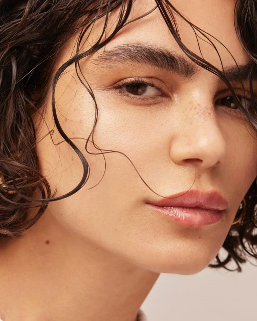 Close-up portrait of an adult female with wet, short, dark hair, fair skin, and light pink lips looking at the camera.