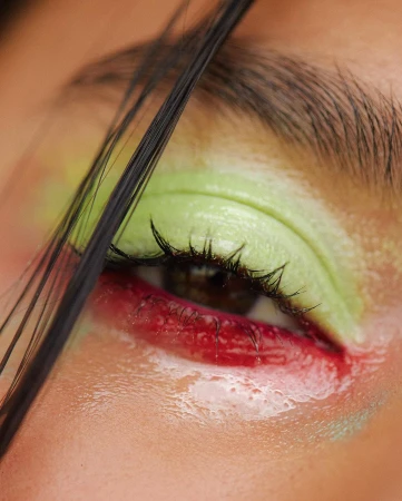 Close-up macro shot of a closed human eye featuring bright green eyeshadow and red pigment on the lower lid by Kayla Varley.