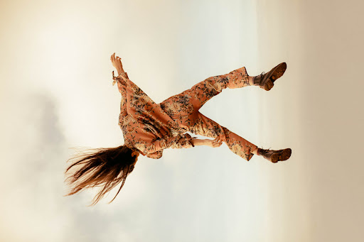Model mid-air in a floral print matching set and dark boots against a pale sky captured by Kayla Varley.