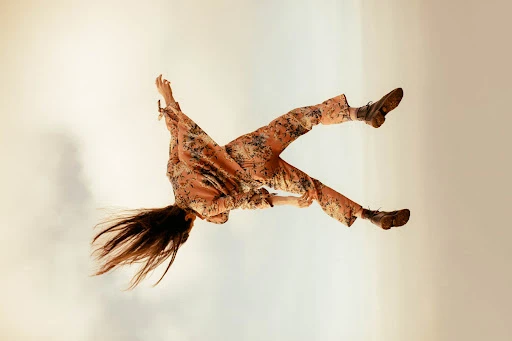 Model mid-air in a floral print matching set and dark boots against a pale sky captured by Kayla Varley.