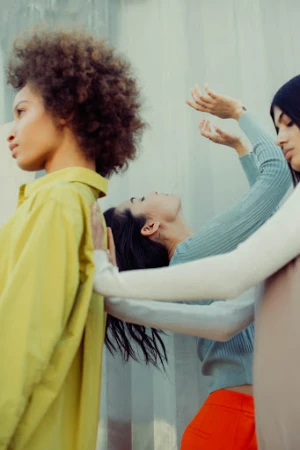 Three female models posing in layered clothing against a translucent fabric backdrop by photographer Kayla Varley