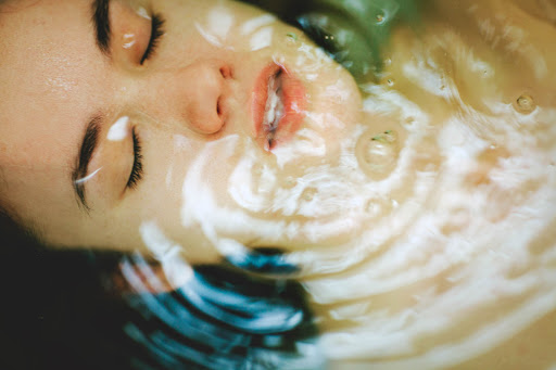 Close-up of a woman's face with her eyes closed submerged in water, capturing ripples and reflections, creating a serene and intimate portrait.