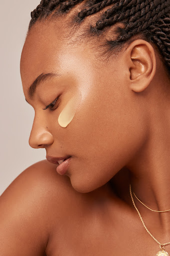 Profile portrait of a Black woman with braided hair wearing a thin gold necklace and concealer on her cheek by Kayla Varley