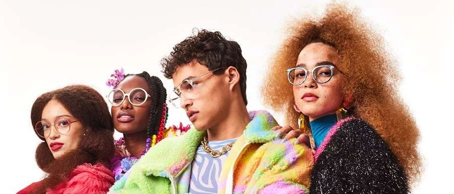 Group of four diverse adults wearing fashionable eyeglasses, colorful clothing, and striking hair styles against a bright white backdrop.