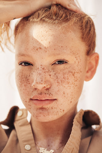 Close-up portrait of a woman with red hair and heavy freckles wearing a tan collared shirt by photographer Kayla Varley.