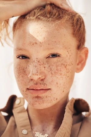 Close-up portrait of a woman with red hair and heavy freckles wearing a tan collared shirt by photographer Kayla Varley.