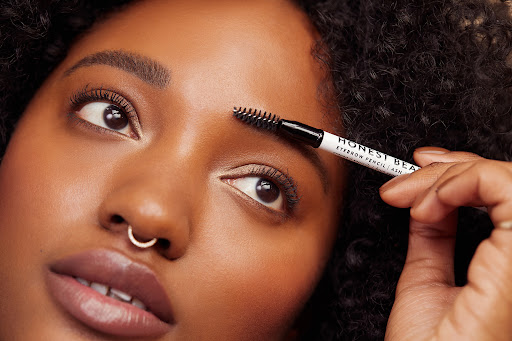 Close-up of a woman with curly hair using an eyebrow brush on her eyebrow. Beauty shot with an eyebrow pencil. Makeup and beauty.