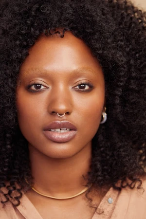 A portrait captures a Black woman in a blue top, smiling softly against a pink and orange background, highlighting her natural hair.