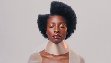 Close-up portrait of a Black woman with eyes closed, styled hair, and a unique tan collar in a brightly lit photo studio.