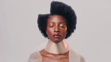 Close-up portrait of a Black woman with eyes closed, styled hair, and a unique tan collar in a brightly lit photo studio.