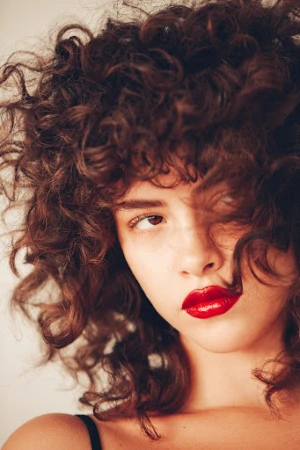 Close-up portrait of a woman with curly brown hair and glossy red lips photographed by Kayla Varley.