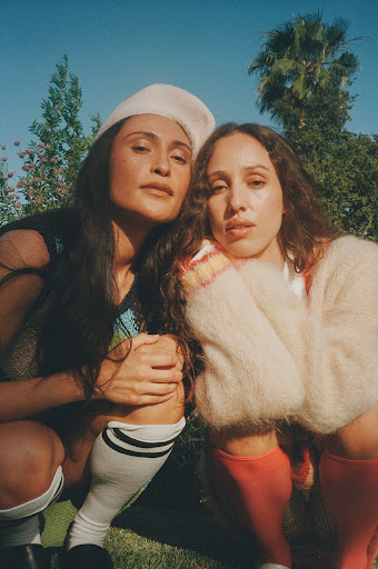 Two women posing outdoors in daylight, wearing knitwear and knee-high socks, photographed by Kayla Varley.