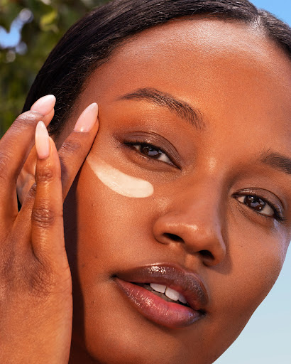 Close-up of an African American woman's face with a streak of cosmetic cream applied under her eye, showcasing beauty and skincare.