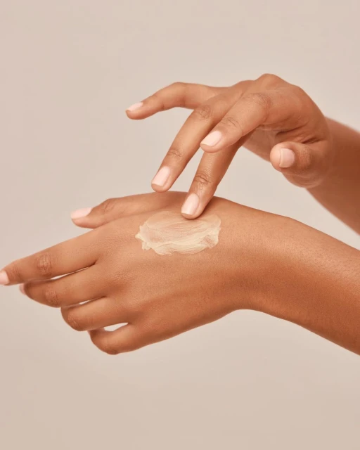 Close-up of dark-skinned hands applying cream, emphasizing skincare, moisturizing, and natural beauty against a neutral backdrop.