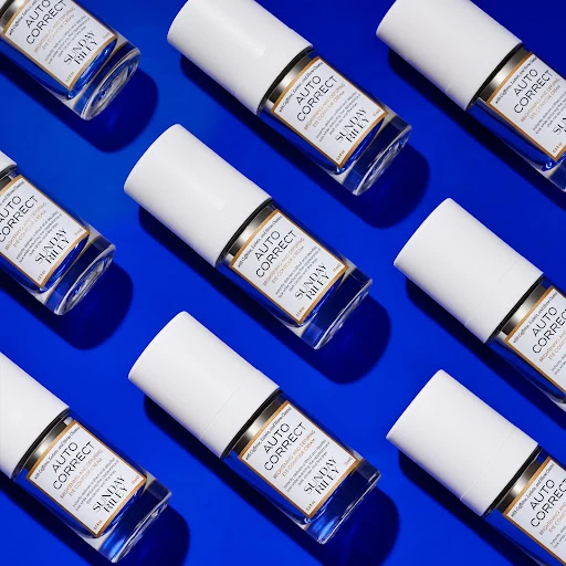 Multiple white tubes of Sunday Riley Auto Correct eye contour cream displayed in a grid pattern against a bright blue background.
