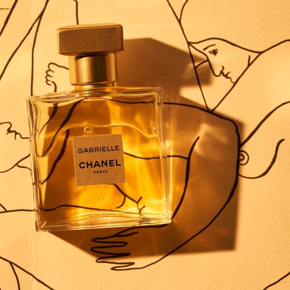 Elegant studio shot of Gabrielle Chanel Paris perfume bottle with gold accents against a sketched nude figure background.