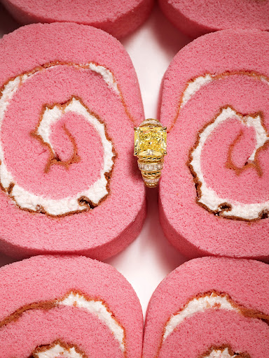 Cushion cut yellow diamond ring displayed atop rows of pink and white Swiss roll cake, macro product photography.