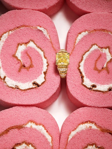 Cushion cut yellow diamond ring displayed atop rows of pink and white Swiss roll cake, macro product photography.