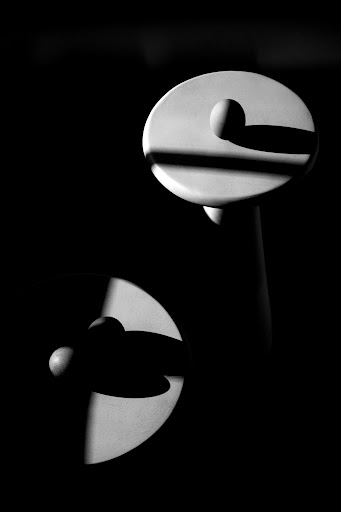 Abstract black and white studio photograph of two white disc-shaped objects and a ball, sharply lit to create strong shadows.