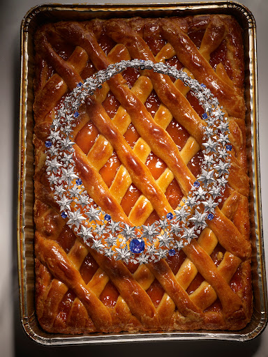 Overhead studio shot of a lattice-crust apricot pie in a metal baking pan with a star-shaped silver and blue gemstone necklace on top.