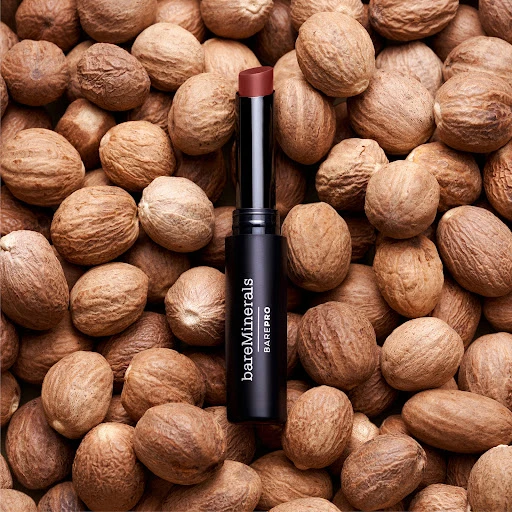 BareMinerals BarePro lipstick in a black tube sits atop a pile of nutmegs, presented in a studio product shot for beauty and fashion.