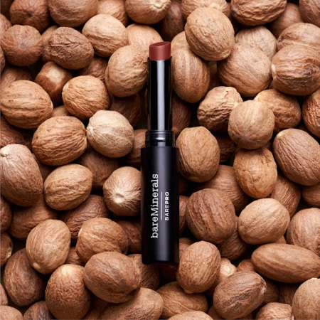 BareMinerals BarePro lipstick in a black tube sits atop a pile of nutmegs, presented in a studio product shot for beauty and fashion.