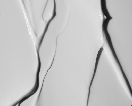 Abstract close-up of a smooth, white cream or lotion with flowing lines and dark shadows creating depth and texture.