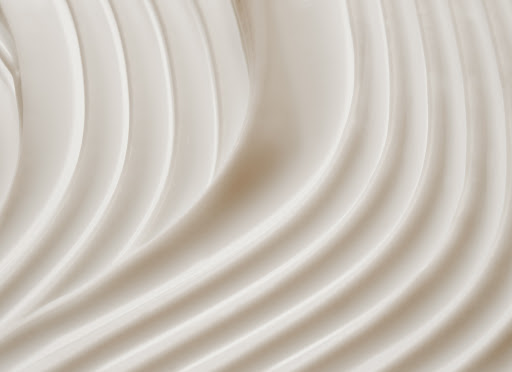 Close-up of thick, rippled, light-beige cream or lotion, creating a smooth, textured surface with soft shadows and highlights.
