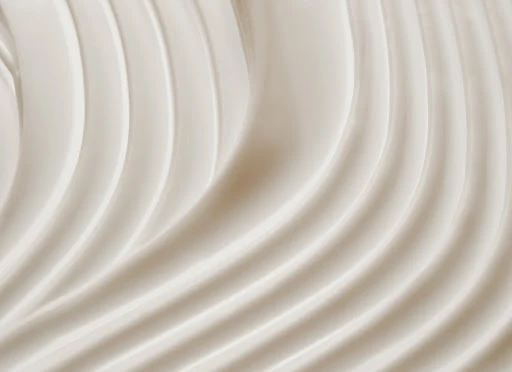 Close-up of thick, rippled, light-beige cream or lotion, creating a smooth, textured surface with soft shadows and highlights.