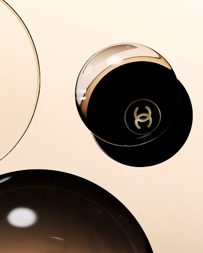 Floating Chanel compact makeup case featuring a gold Chanel logo against a soft gradient background, with transparent circles creating depth.
