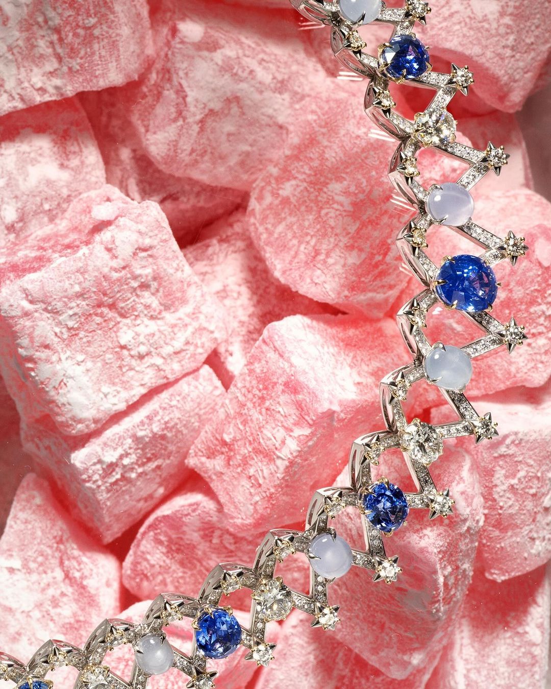 High-angle view of a silver-tone necklace with blue and white stones, displayed on a textured surface of light-pink Turkish delight candy.