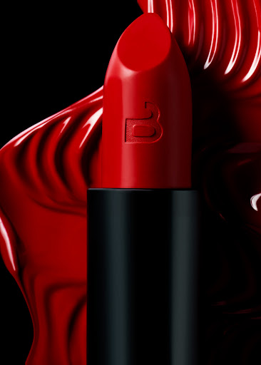 Close-up of vibrant red lipstick with a sleek black case, set against a dramatic backdrop of matching red cosmetic swirl.