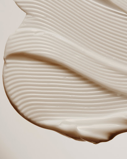 Close-up of textured white cream with wavy lines and a smooth finish against a plain background, highlighting skincare or cosmetic product.