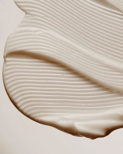 Close-up of textured white cream with wavy lines and a smooth finish against a plain background, highlighting skincare or cosmetic product.