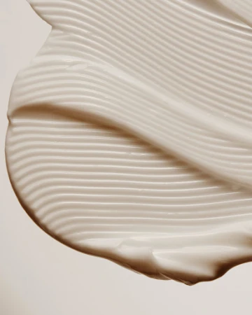 Close-up of textured white cream with wavy lines and a smooth finish against a plain background, highlighting skincare or cosmetic product.