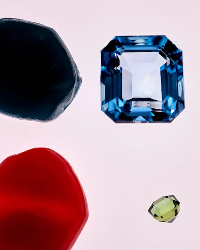 Close-up of blue, green, red, and dark blue gemstones with different cuts on a light background, perfect for jewelry designs.