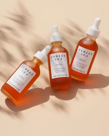 Three bottles of Tyrion Sea antioxidant facial oil by Skinvolve are arranged against a light beige background with shadow from foliage.