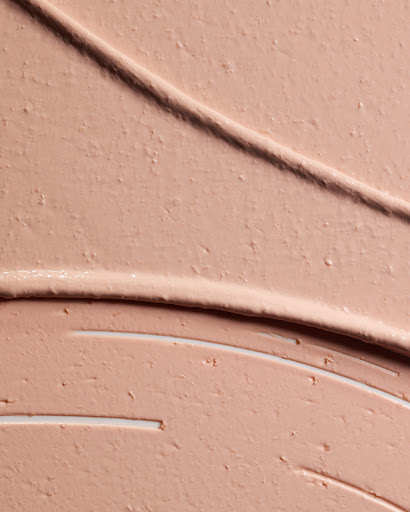 Close-up of thick, creamy beige cosmetic foundation or moisturizer, swiped unevenly across a surface, showing texture and depth.