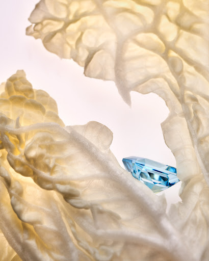 Macro photograph of a translucent blue gemstone resting on textured, pale lettuce leaves, creating a striking contrast of color and form.