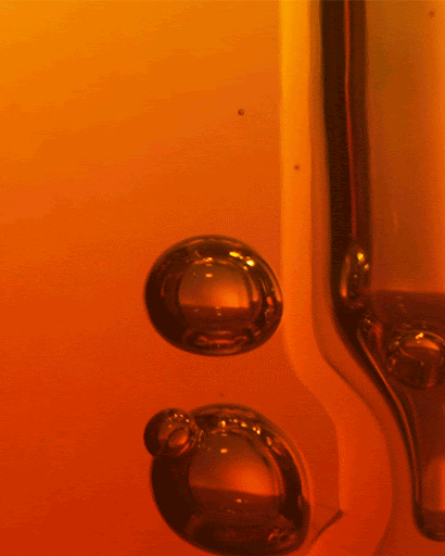 Close-up of two translucent bubbles in a gradient orange liquid, with a vertical glass tube along the right edge.