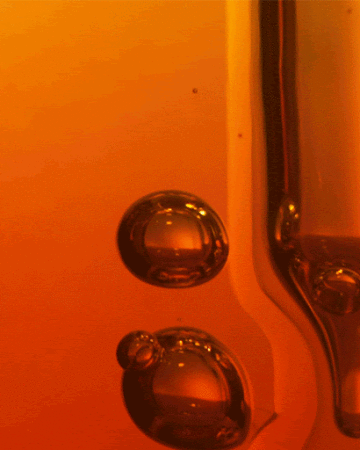 Close-up of two translucent bubbles in a gradient orange liquid, with a vertical glass tube along the right edge.