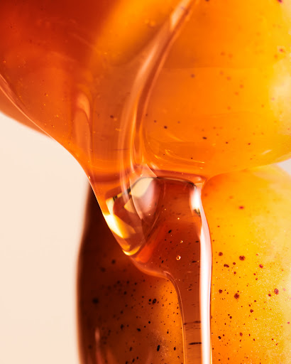 Close-up of honey dripping from a golden grape, showcasing the liquid's texture and color, ideal for food and beverage visuals.