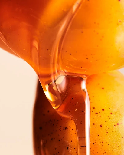 Close-up of honey dripping from a golden grape, showcasing the liquid's texture and color, ideal for food and beverage visuals.