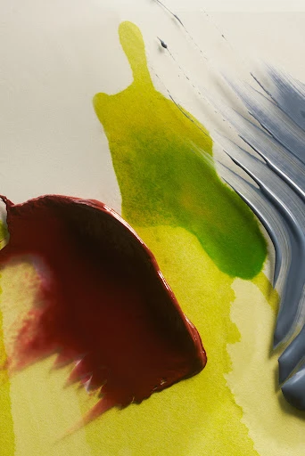 Abstract art featuring a combination of grey, yellow, green, and maroon paint streaks against a white background, close-up view.