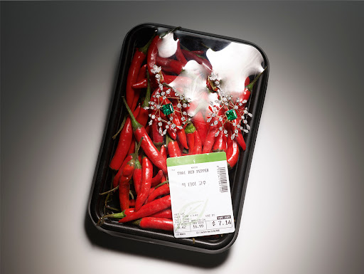 Close-up of red chili peppers arranged in a black plastic tray, adorned with silver and emerald jewelry, under studio lighting.