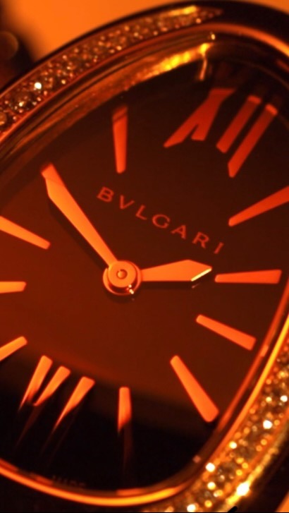 Close-up of a Bulgari watch with a black face, Roman numerals, and a diamond-encrusted bezel under warm lighting.
