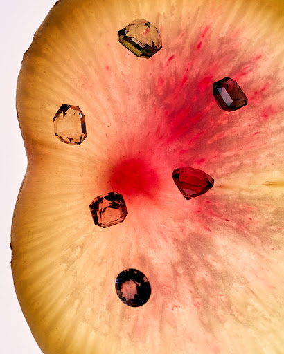 Arrangement of six raw gemstone jewels on a light yellow and red translucent mineral slice, studio lighting, bright color palette.